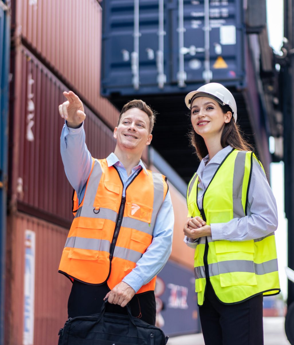 Caucasian business man and woman worker working in container terminal.  Attractive engineer people processes orders and product at warehouse logistic in cargo freight ship for import export in harbor.