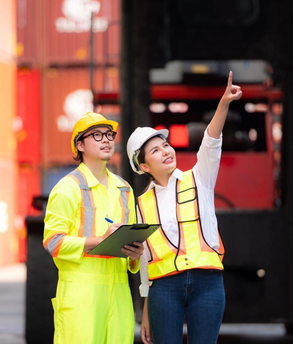 Portrait of Asian woman engineer and worker working with co-worker at overseas shipping container yard.